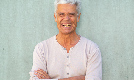 happy older man laughing with arms crossed by green wall