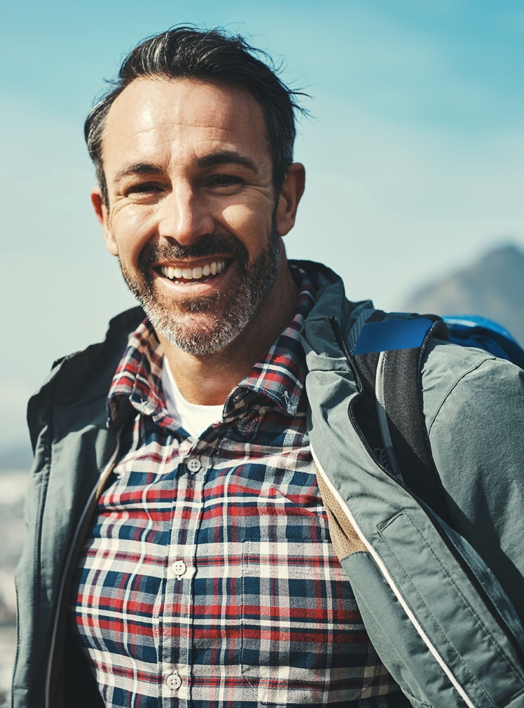 Smiles are forms of happiness found right under our noses. Portrait of a middle aged man smiling in front of a mountain landscape.